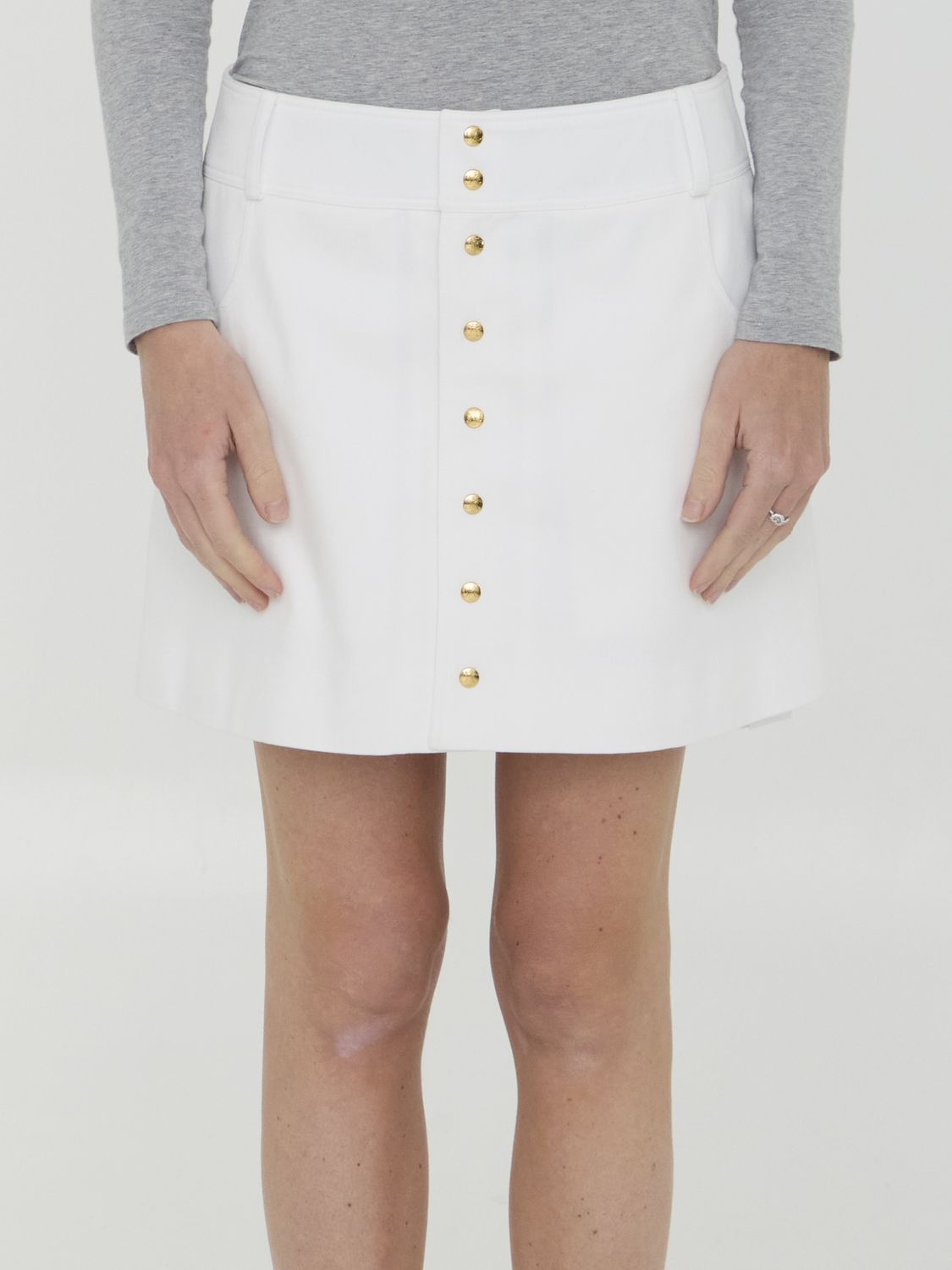 تنورة قصيرة بيضاء مصنوعة من القطن مزودة بأزرار معدنية ذهبية - قطعة أزياء نسائية
